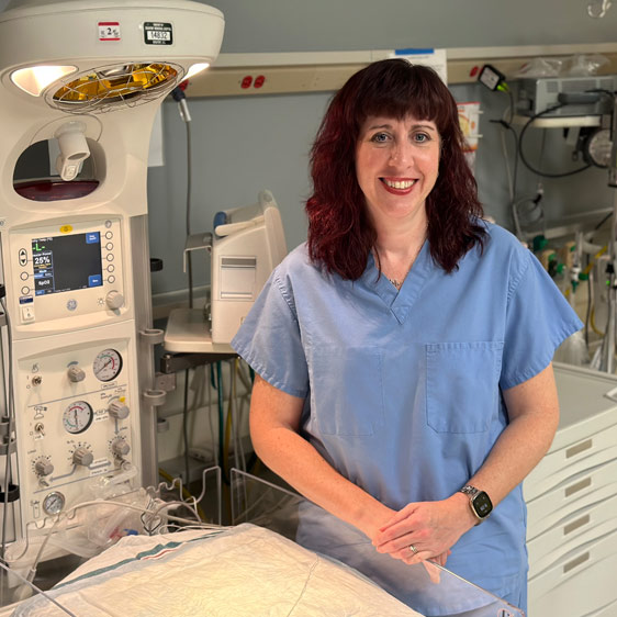 A nurse named Carrie McClure dressed in blue scrubs and sitting in front of medical equipment for a photograph