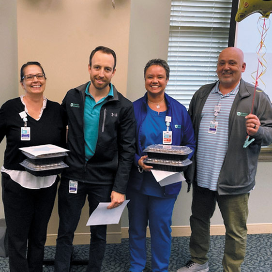 Four hospital employees wearing their badges and smiling for the camera