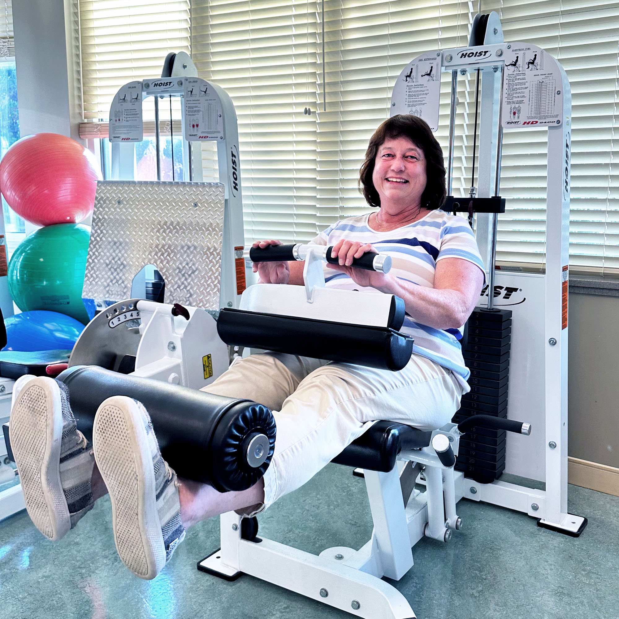 Ashley Sanders smiles while using a leg extension machine at the physical therapy gym