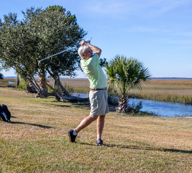 An older man wearing shorts and a green shirt hits a golf ball.