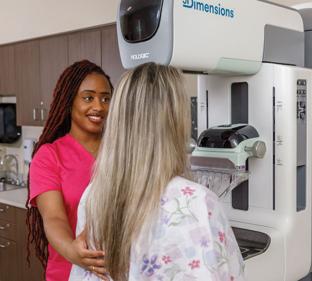 Woman receiving a mammogram from a medical professional in pink scrubs