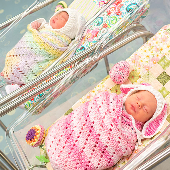 An infant in a bassinet wrapped in a crocheted pink blanket