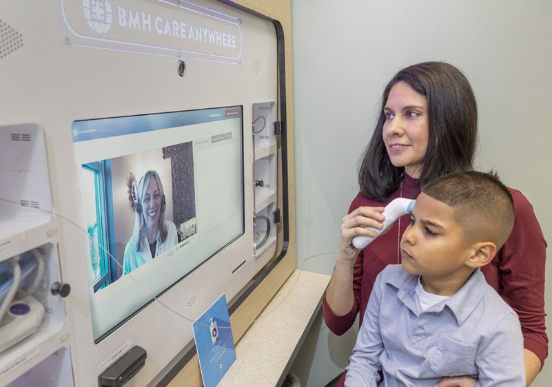 woman using a thermometer on her son at a BMH Care Anywhere video kiosk