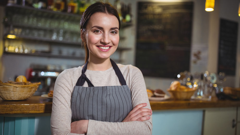 A woman smiling wearing an apron with her arms crossed