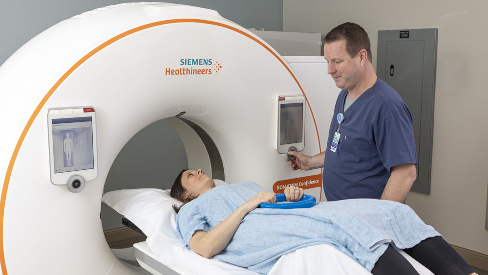 technologist making sure a patient is comfortable before starting a CT scan