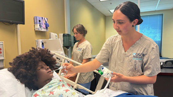 nursing student takes temperature of simulation manikin